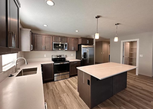 kitchen featuring a kitchen island, light wood-type flooring, light countertops, appliances with stainless steel finishes, and a sink