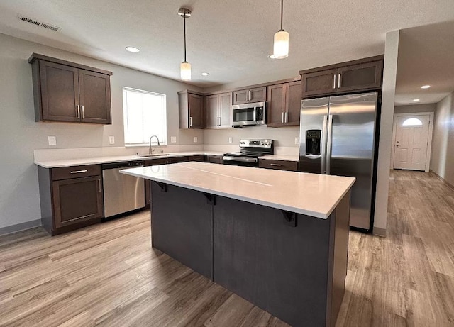 kitchen with visible vents, dark brown cabinetry, light wood-style flooring, a kitchen breakfast bar, and stainless steel appliances