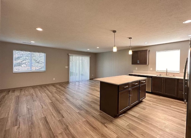 kitchen featuring dark brown cabinetry, open floor plan, light countertops, light wood-style floors, and a textured ceiling