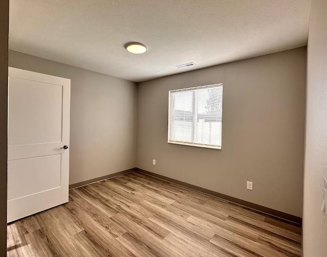 unfurnished room with light wood-style flooring, baseboards, visible vents, and a textured ceiling