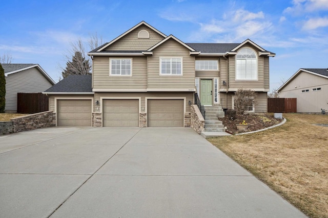 raised ranch with stone siding, an attached garage, concrete driveway, and fence