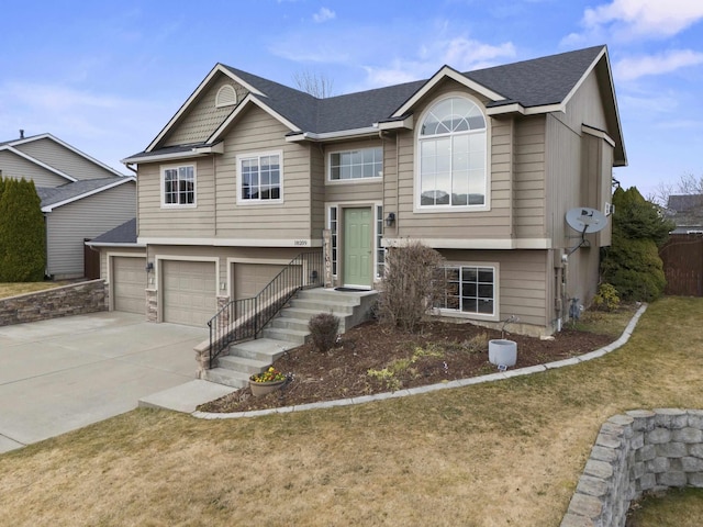 bi-level home featuring an attached garage, driveway, and a shingled roof