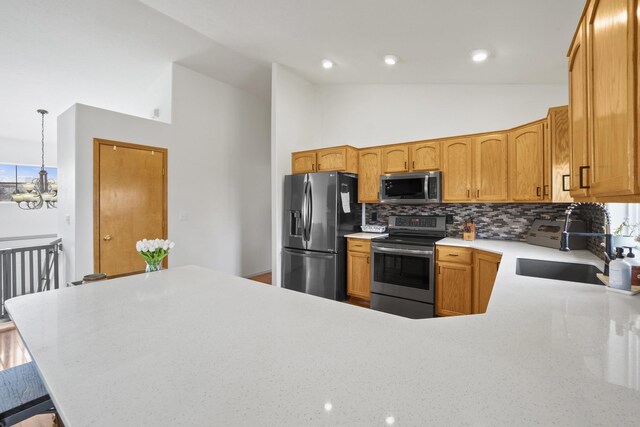 kitchen with a peninsula, a sink, appliances with stainless steel finishes, a notable chandelier, and backsplash