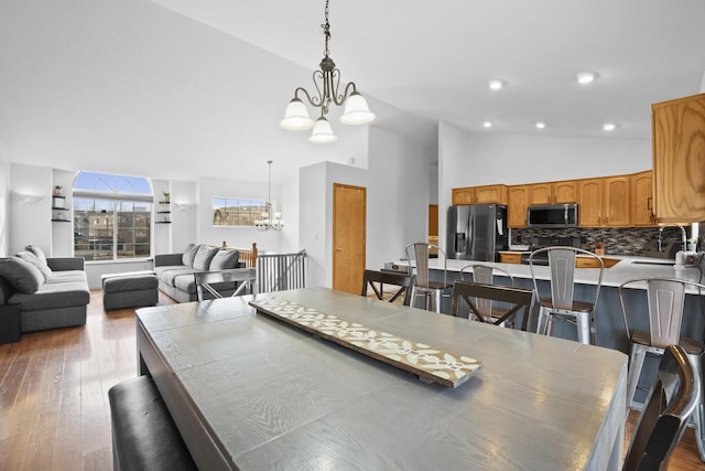 dining space featuring recessed lighting, wood-type flooring, a notable chandelier, and high vaulted ceiling