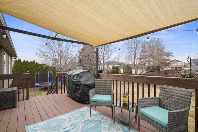 wooden terrace featuring grilling area, a trampoline, and fence