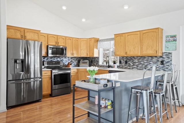 kitchen with vaulted ceiling, appliances with stainless steel finishes, a peninsula, light wood-style floors, and a sink