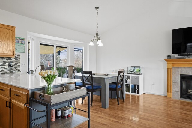 dining area with light wood finished floors, a chandelier, a fireplace, and vaulted ceiling