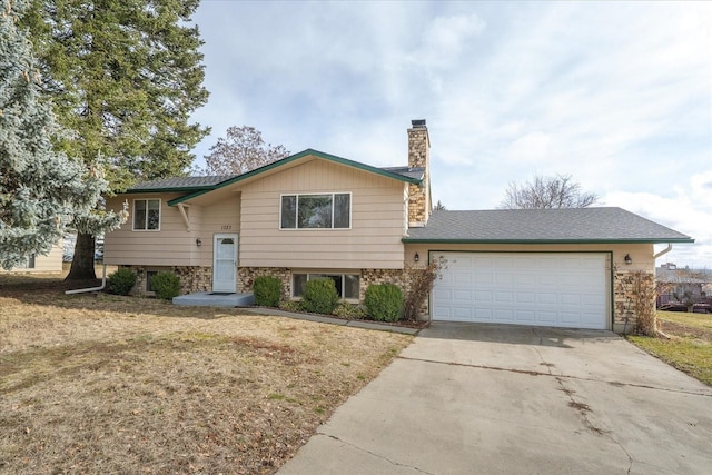 split foyer home featuring concrete driveway, a garage, stone siding, and a chimney