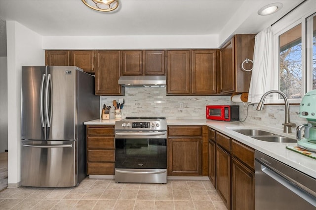 kitchen with under cabinet range hood, stainless steel appliances, light countertops, and a sink