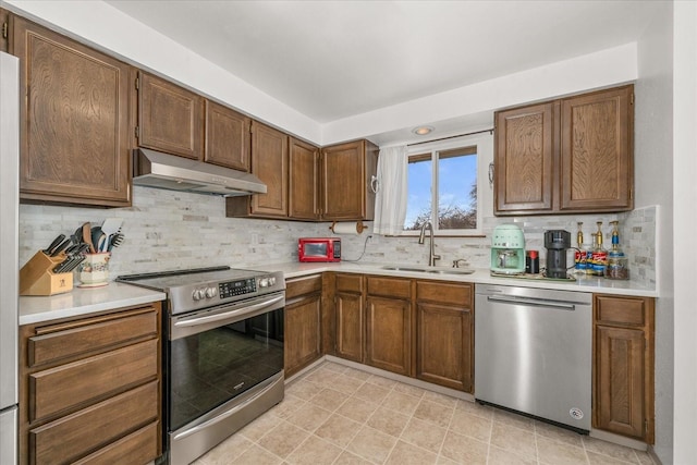 kitchen with a sink, light countertops, under cabinet range hood, appliances with stainless steel finishes, and backsplash