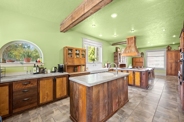 kitchen with a sink, beamed ceiling, plenty of natural light, and an island with sink