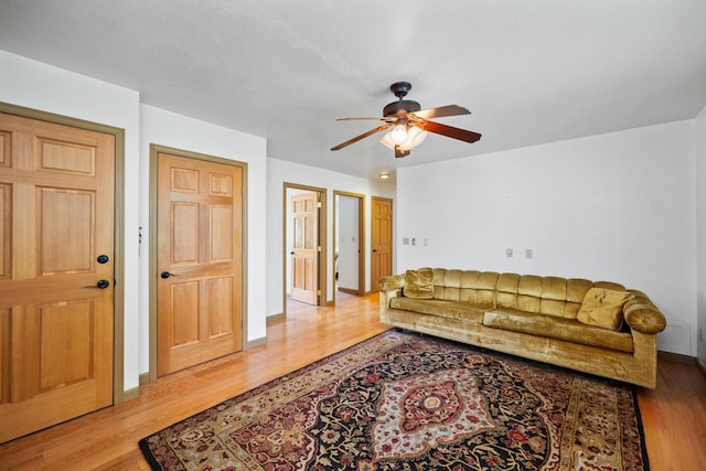 living area featuring baseboards, a ceiling fan, and wood finished floors