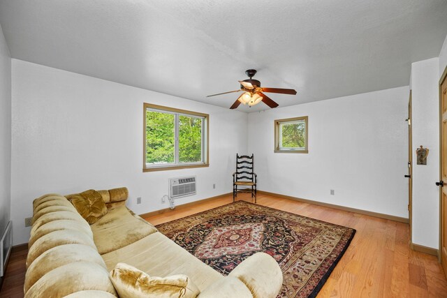 living area featuring wood finished floors, baseboards, a wall mounted air conditioner, and ceiling fan