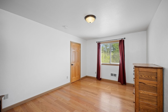 empty room with light wood-style floors, visible vents, and baseboards