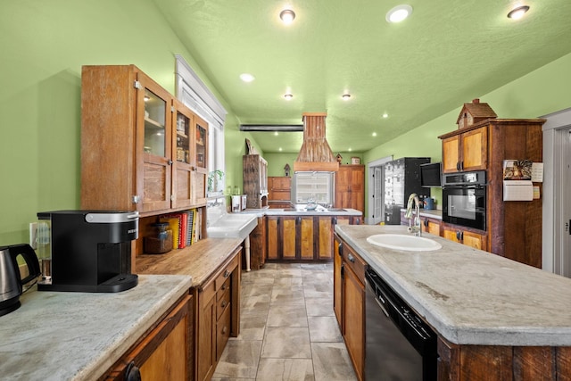 kitchen featuring dishwashing machine, brown cabinetry, a center island with sink, a sink, and black oven