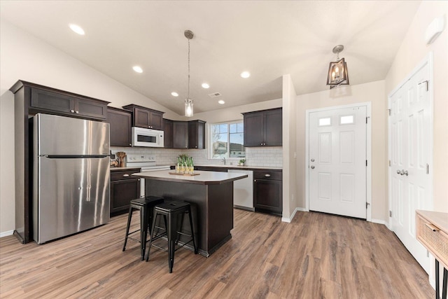 kitchen with a kitchen island, a breakfast bar, light wood-type flooring, vaulted ceiling, and white appliances