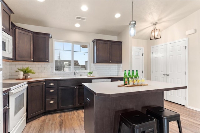 kitchen featuring white appliances, visible vents, dark brown cabinetry, and a sink