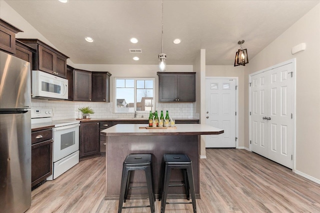 kitchen featuring a kitchen bar, light wood-style flooring, a kitchen island, white appliances, and dark brown cabinetry