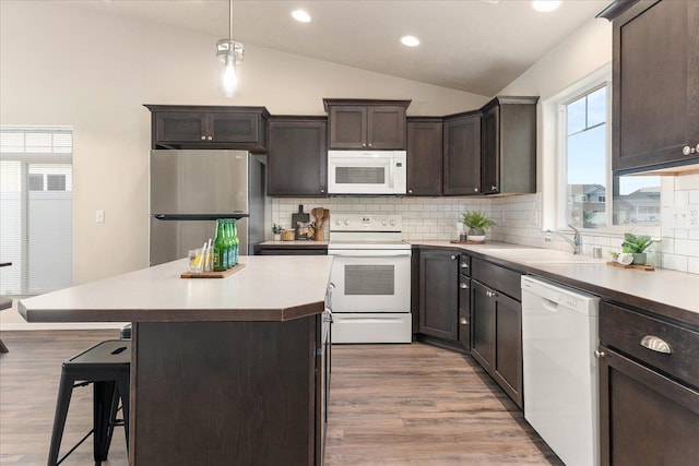 kitchen featuring a sink, a kitchen breakfast bar, white appliances, dark brown cabinetry, and vaulted ceiling