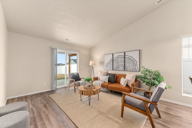 living room with vaulted ceiling, visible vents, light wood-type flooring, and baseboards