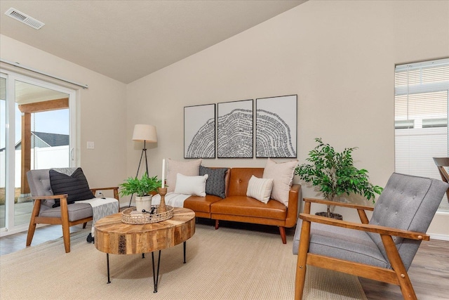 living area with visible vents, light wood-style floors, and vaulted ceiling