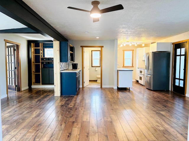 kitchen with dark wood-type flooring, baseboards, light countertops, freestanding refrigerator, and a textured ceiling