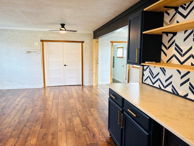 kitchen featuring open shelves, a textured ceiling, hardwood / wood-style floors, and dark cabinets