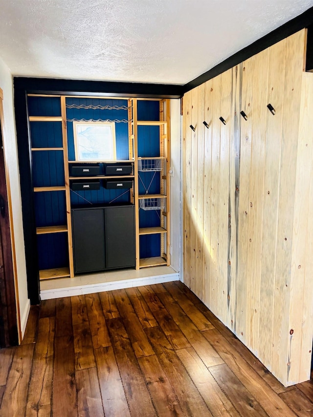 unfurnished room with wooden walls, a textured ceiling, and hardwood / wood-style floors