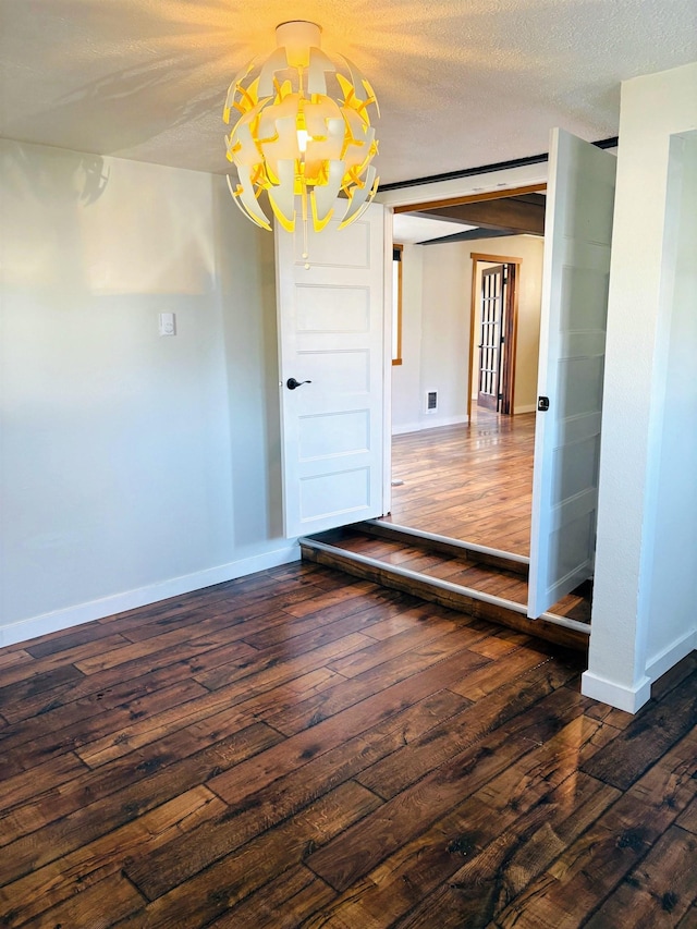 empty room featuring hardwood / wood-style flooring, baseboards, a chandelier, and a textured ceiling