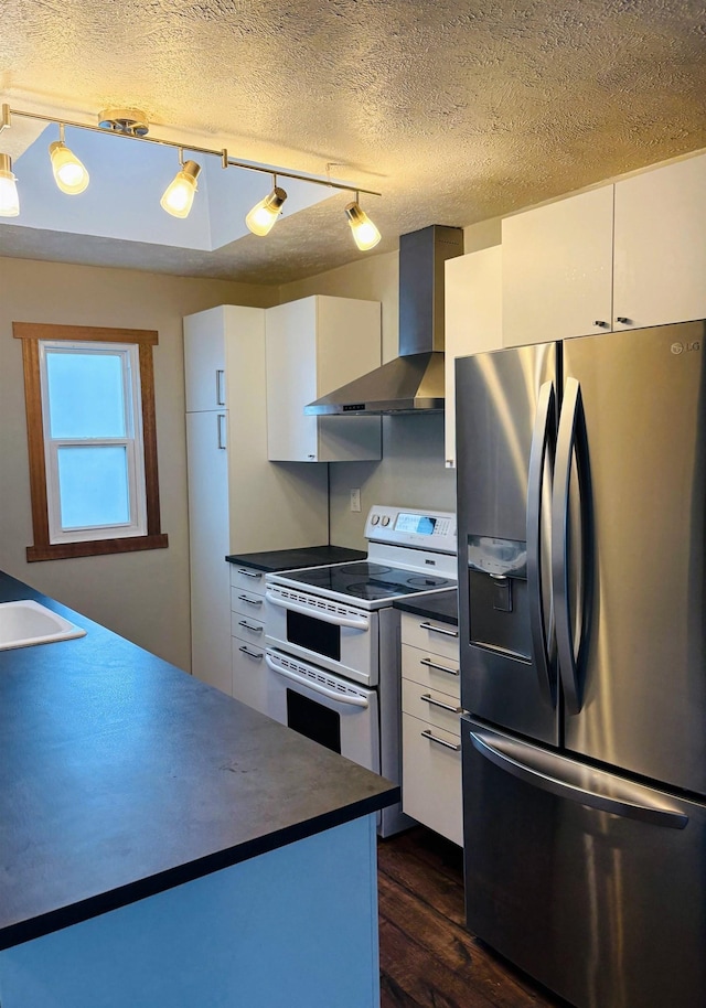 kitchen featuring stainless steel refrigerator with ice dispenser, dark countertops, wall chimney exhaust hood, range with two ovens, and dark wood-style flooring