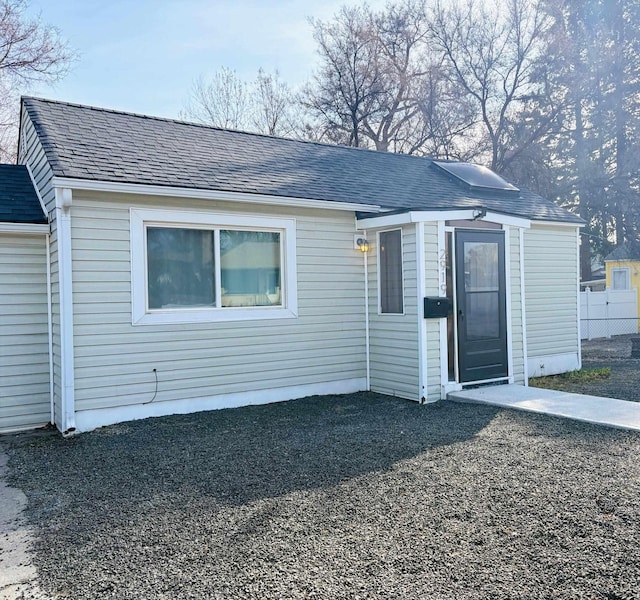 view of front facade featuring roof with shingles and fence