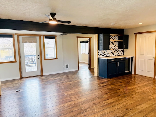 unfurnished living room featuring visible vents, a textured ceiling, dark wood-type flooring, and baseboards