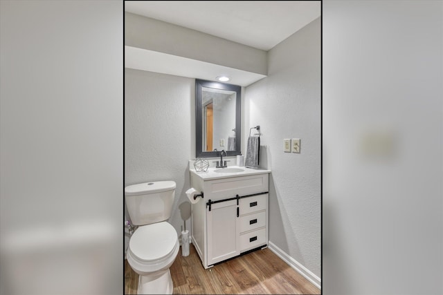 bathroom with baseboards, toilet, wood finished floors, and a textured wall