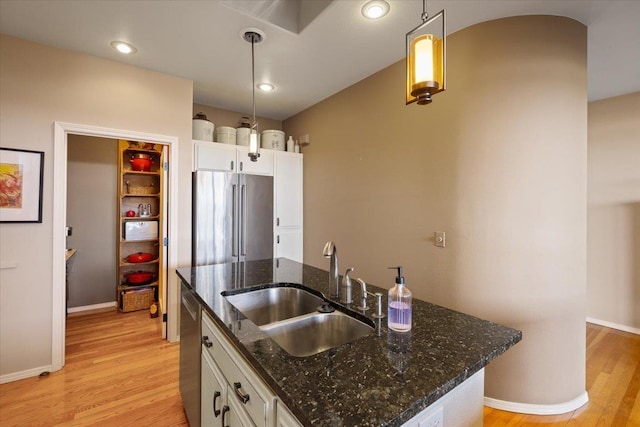 kitchen featuring pendant lighting, a kitchen island with sink, a sink, stainless steel appliances, and light wood-style floors