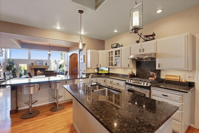 kitchen featuring light wood finished floors, stainless steel range with gas cooktop, a lit fireplace, a sink, and under cabinet range hood