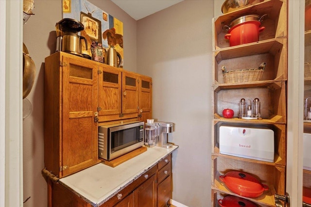 kitchen featuring stainless steel microwave, brown cabinets, light countertops, and open shelves