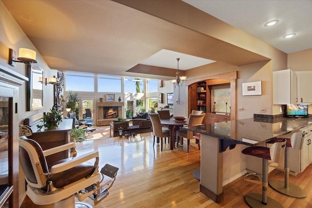 interior space with a chandelier, a kitchen bar, light wood-type flooring, a warm lit fireplace, and white cabinets