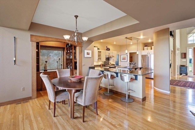 dining space with light wood finished floors, a chandelier, baseboards, and visible vents