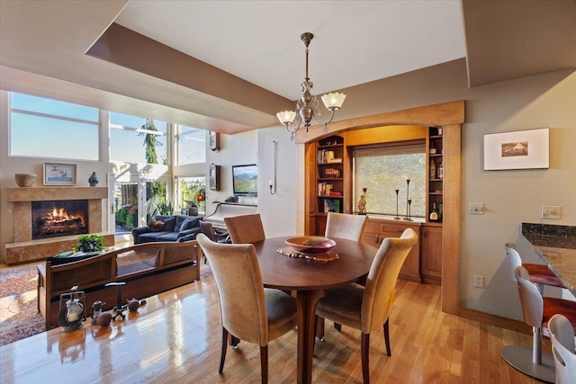 dining area with light wood finished floors, a fireplace, baseboards, and an inviting chandelier