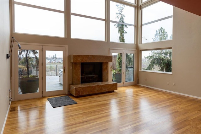 unfurnished living room with wood finished floors, a towering ceiling, french doors, and a high end fireplace