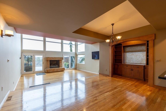 unfurnished living room with visible vents, baseboards, a chandelier, a premium fireplace, and light wood-style floors