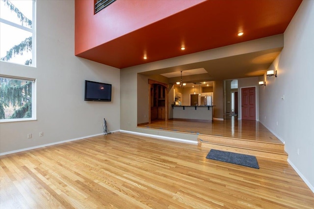 unfurnished living room featuring baseboards, a chandelier, recessed lighting, a high ceiling, and wood finished floors