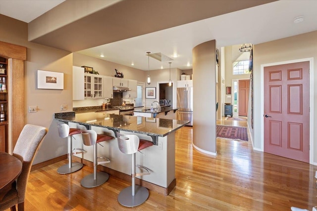 kitchen with under cabinet range hood, a breakfast bar, light wood-type flooring, appliances with stainless steel finishes, and a peninsula