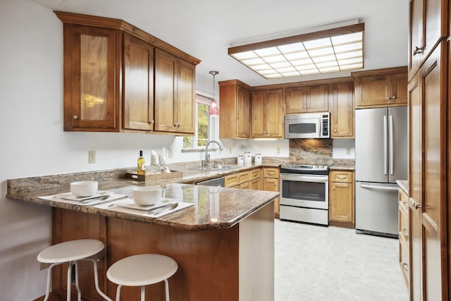 kitchen with pendant lighting, a sink, appliances with stainless steel finishes, a peninsula, and light floors