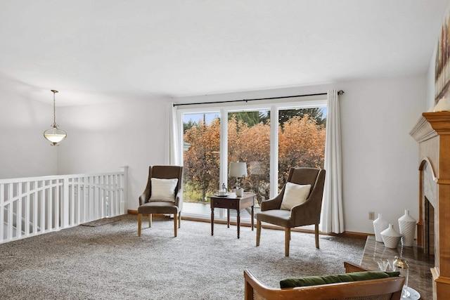 sitting room featuring baseboards, a fireplace with raised hearth, and carpet flooring