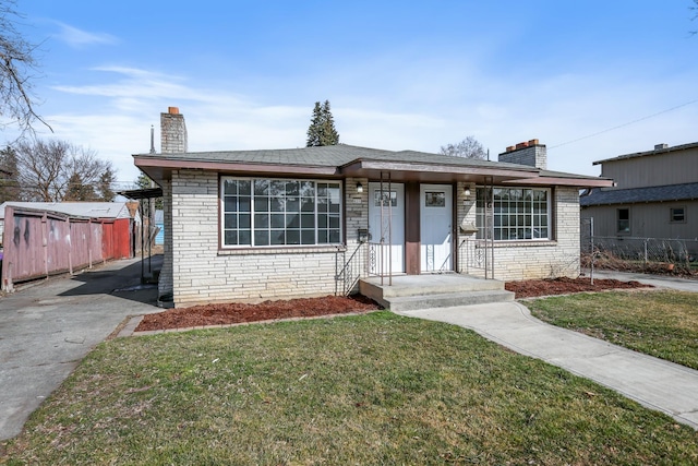 view of front of house with brick siding, a chimney, a front yard, and fence