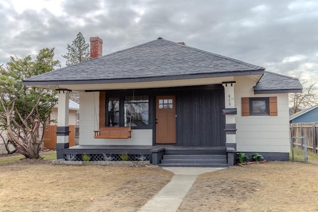 view of front of property featuring a chimney, covered porch, a shingled roof, and fence