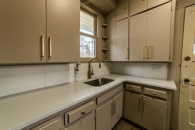 kitchen featuring backsplash, gray cabinetry, light countertops, and a sink