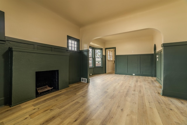 unfurnished living room with a wainscoted wall, visible vents, light wood-style flooring, a fireplace, and arched walkways