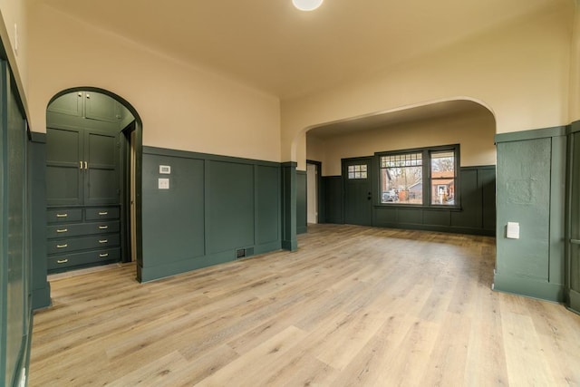 spare room with visible vents, arched walkways, light wood-style floors, and wainscoting